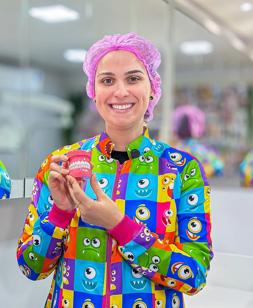 Dra. Bárbara Menegat sorrindo no consultório e segurando um modelo odontológico